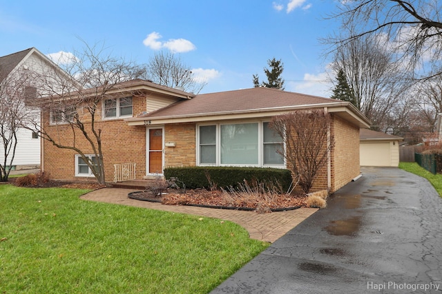 tri-level home featuring a garage, a front lawn, an outbuilding, and brick siding