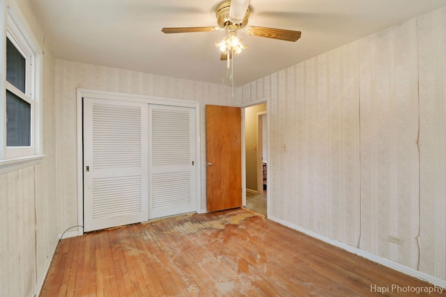 unfurnished bedroom with a closet, wood-type flooring, baseboards, and wallpapered walls