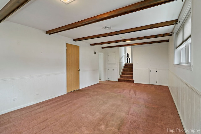 carpeted spare room with a wainscoted wall, stairway, and beam ceiling