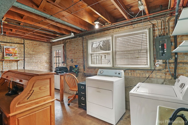 laundry room with laundry area, electric panel, washer and clothes dryer, and brick wall