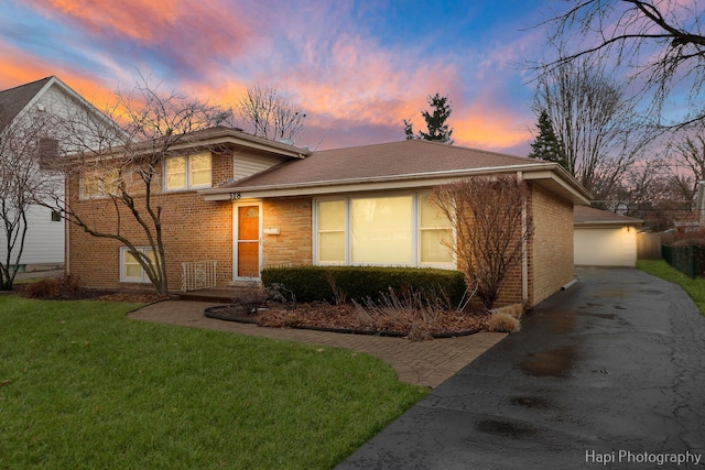 tri-level home featuring a garage, an outbuilding, brick siding, and a yard