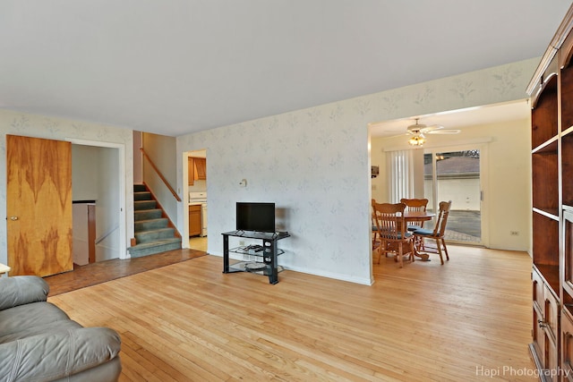 living room with a ceiling fan, baseboards, stairs, light wood-type flooring, and wallpapered walls