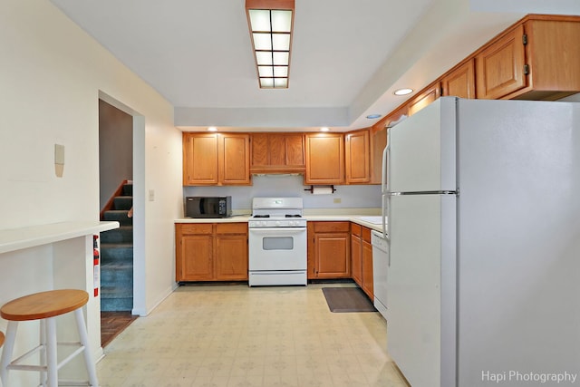 kitchen featuring white appliances, brown cabinetry, light countertops, light floors, and recessed lighting