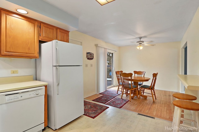 kitchen featuring white appliances, visible vents, a ceiling fan, light floors, and brown cabinetry