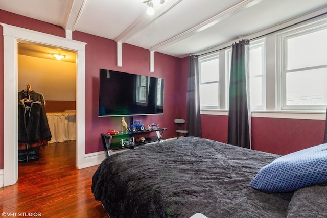 bedroom with wood finished floors, beam ceiling, and baseboards