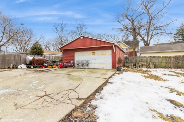 snow covered garage featuring a detached garage and fence