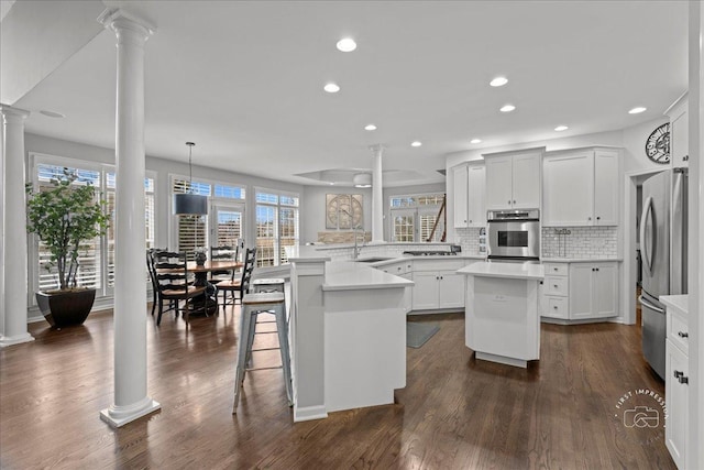 kitchen featuring a kitchen island, dark wood-type flooring, a peninsula, stainless steel appliances, and ornate columns