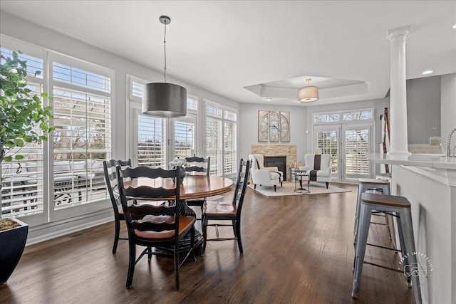 dining space featuring dark wood-style floors, a raised ceiling, a fireplace, and decorative columns