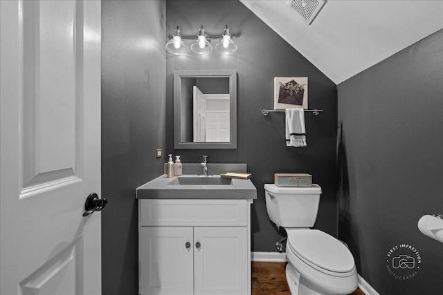 half bath with lofted ceiling, visible vents, toilet, vanity, and wood finished floors