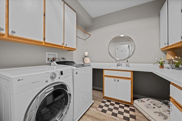 clothes washing area featuring a sink, light wood finished floors, washing machine and clothes dryer, and cabinet space