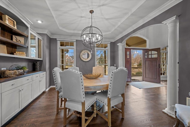 dining room featuring a notable chandelier, dark wood-style floors, a tray ceiling, decorative columns, and crown molding