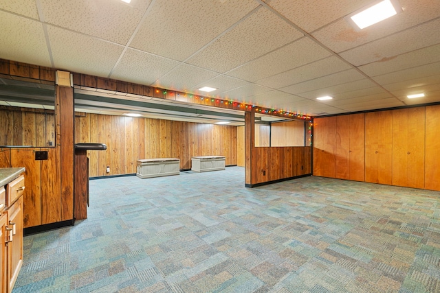 finished below grade area with carpet, a paneled ceiling, and wooden walls