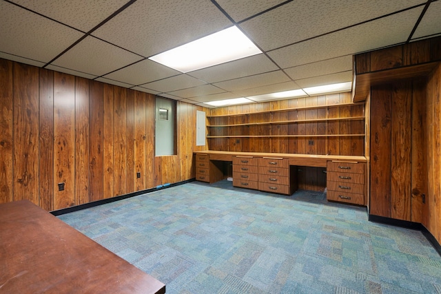 unfurnished office featuring carpet floors, a drop ceiling, wood walls, and built in desk