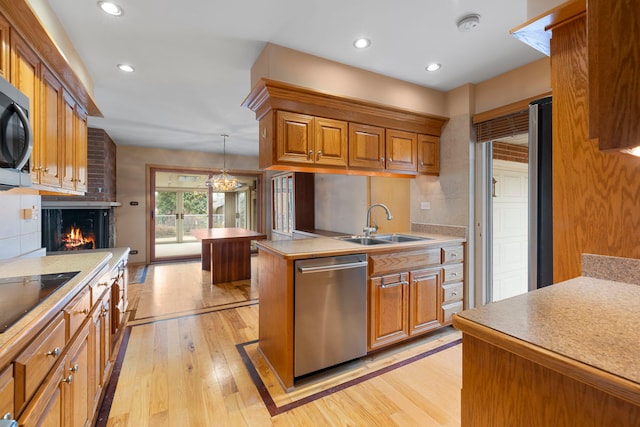 kitchen with light wood-style flooring, appliances with stainless steel finishes, brown cabinets, a fireplace, and a sink