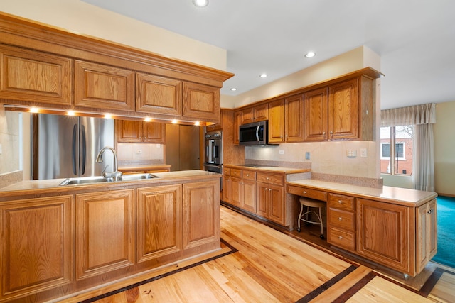 kitchen featuring a peninsula, brown cabinetry, stainless steel appliances, and a sink