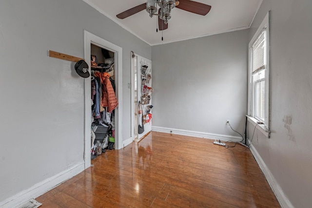 empty room with a ceiling fan, wood-type flooring, crown molding, and baseboards