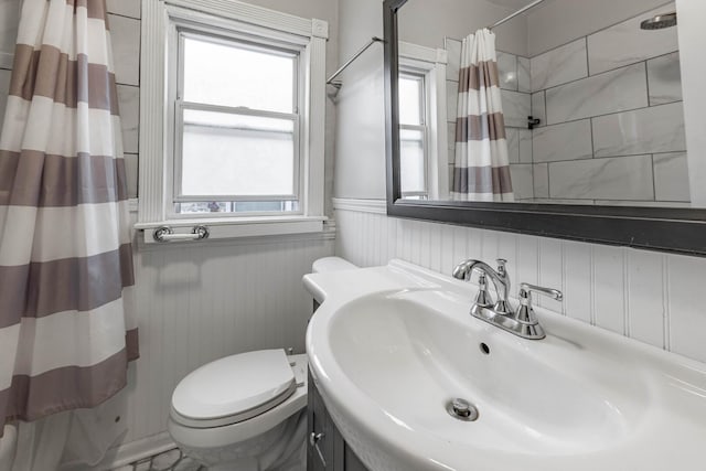 full bathroom featuring a shower with shower curtain, wainscoting, a sink, and toilet