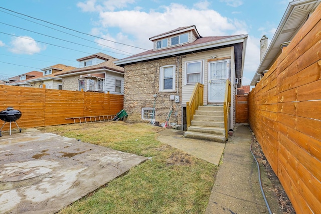 rear view of house with entry steps, a patio, brick siding, fence, and a lawn