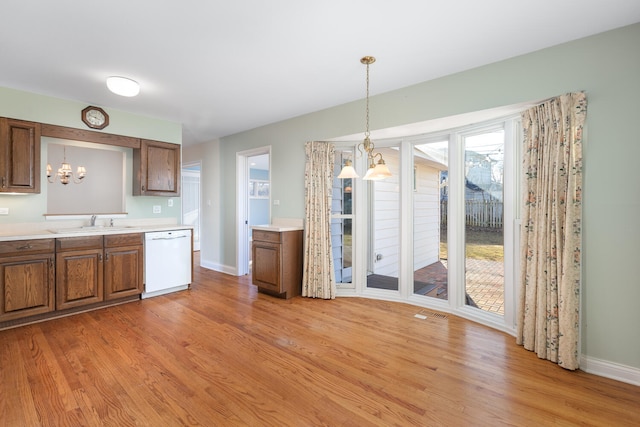 kitchen featuring brown cabinetry, light wood finished floors, an inviting chandelier, a sink, and dishwasher