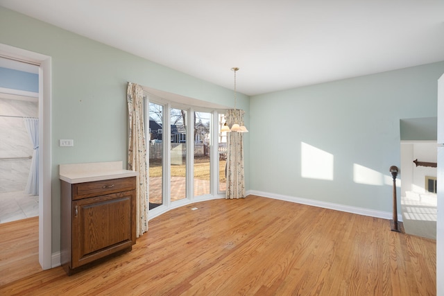 unfurnished dining area with a notable chandelier, baseboards, and light wood finished floors