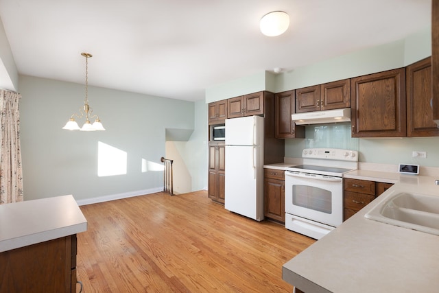 kitchen featuring white appliances, a sink, light countertops, under cabinet range hood, and light wood-type flooring