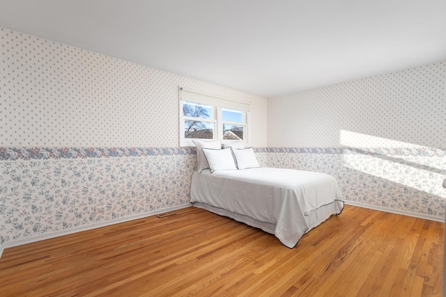 bedroom featuring light wood finished floors, visible vents, wallpapered walls, and baseboards