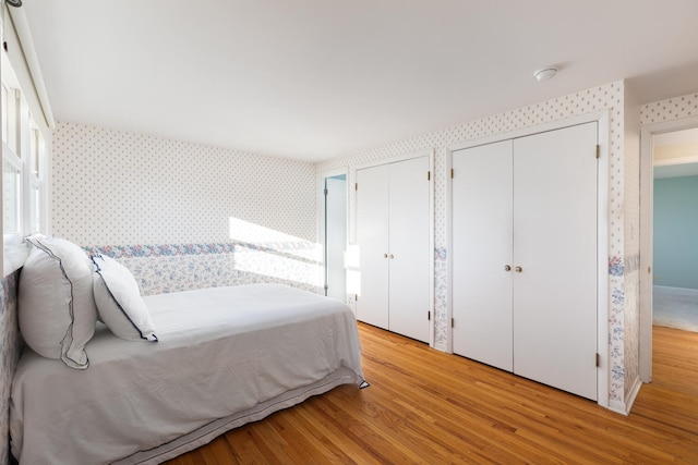 bedroom featuring wallpapered walls, multiple closets, and light wood finished floors