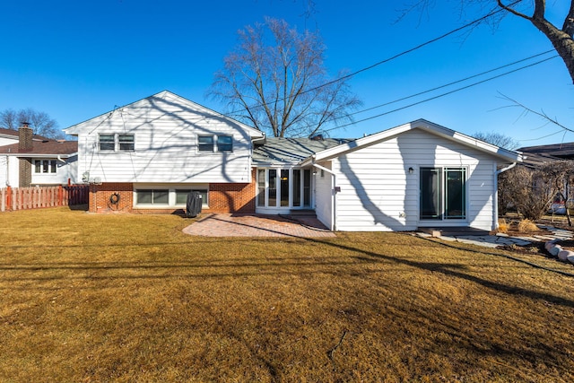 back of house with brick siding, a lawn, and fence