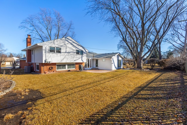 back of property with brick siding, a chimney, central air condition unit, a patio area, and a lawn