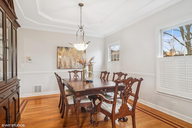 dining room with light wood-type flooring, a raised ceiling, visible vents, and a healthy amount of sunlight