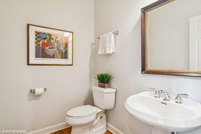 half bathroom featuring toilet, baseboards, and a sink