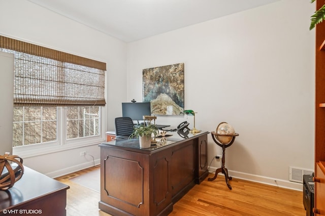 home office with light wood finished floors, visible vents, and baseboards