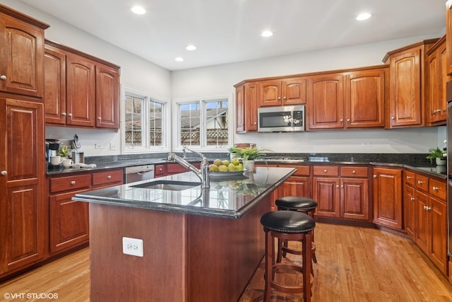 kitchen with stainless steel appliances, light wood finished floors, a sink, and a kitchen breakfast bar