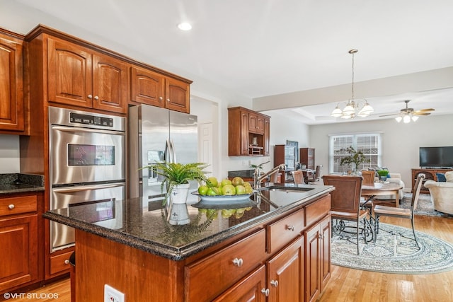 kitchen featuring stainless steel appliances, open floor plan, dark stone counters, a sink, and light wood-type flooring