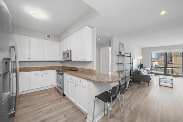 kitchen featuring appliances with stainless steel finishes, open floor plan, white cabinetry, light wood-type flooring, and a kitchen breakfast bar