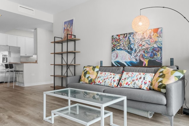 living room with light wood-type flooring, visible vents, and baseboards