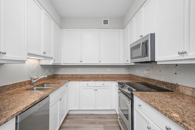 kitchen with light wood-style flooring, stainless steel appliances, a sink, visible vents, and white cabinets