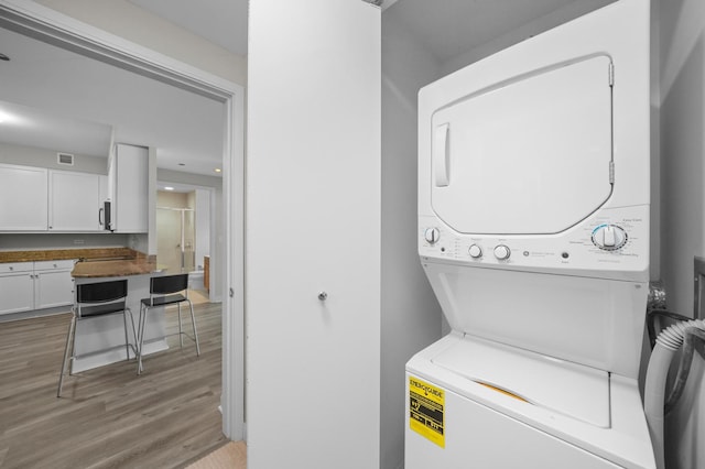 laundry area with laundry area, light wood-style flooring, visible vents, and stacked washer and clothes dryer