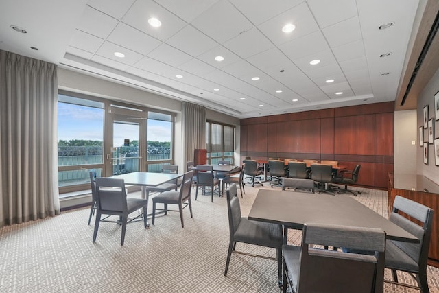 dining room featuring recessed lighting, a raised ceiling, light carpet, and wooden walls