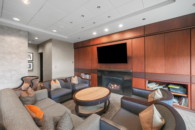 living room with recessed lighting, a raised ceiling, a drop ceiling, and a glass covered fireplace