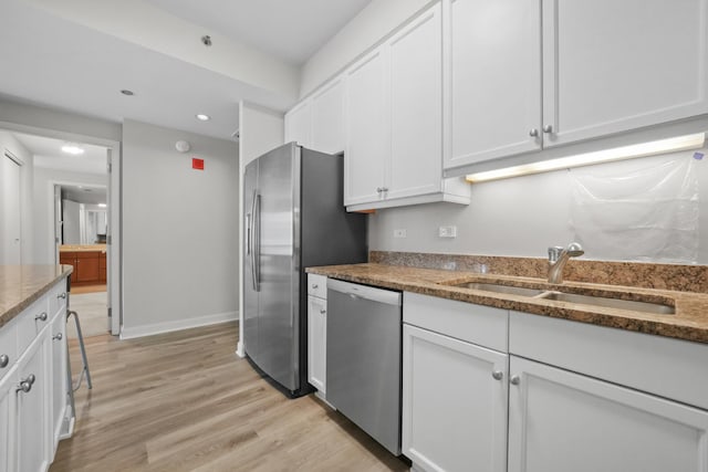 kitchen with light wood finished floors, stainless steel appliances, white cabinetry, a sink, and dark stone countertops