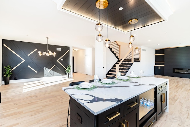 kitchen featuring light wood finished floors, hanging light fixtures, open floor plan, a kitchen island, and dark cabinets