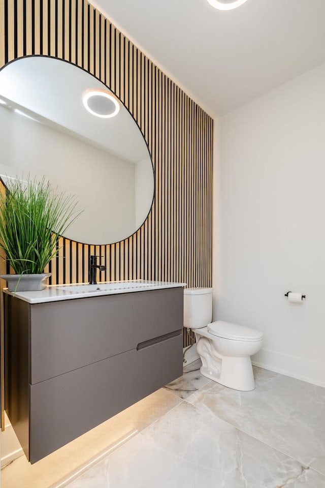 bathroom featuring toilet, marble finish floor, baseboards, and vanity