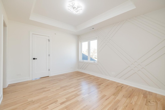 spare room featuring ornamental molding, a tray ceiling, light wood-type flooring, and baseboards