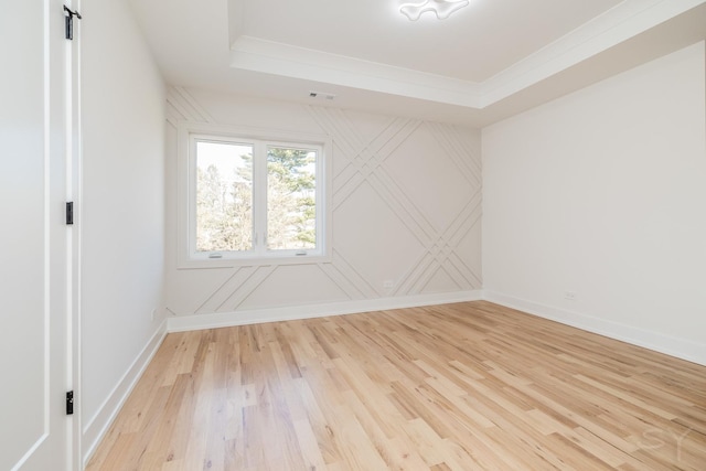 spare room with light wood-type flooring, a tray ceiling, and baseboards