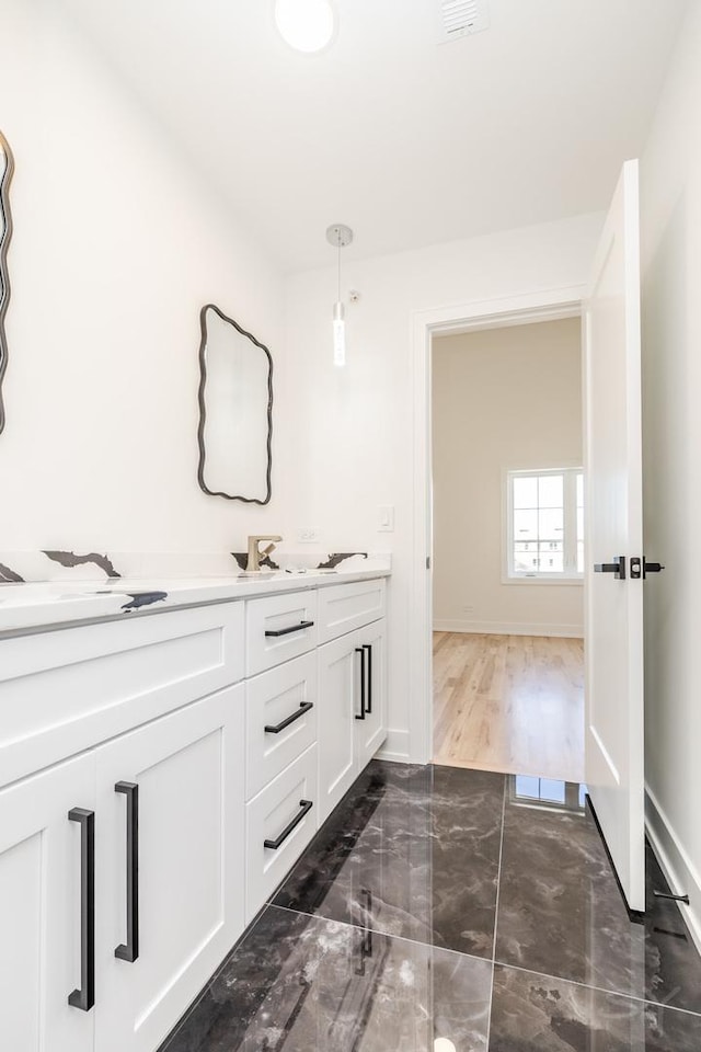 bathroom featuring marble finish floor, double vanity, a sink, and baseboards