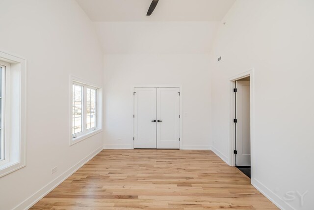 unfurnished room featuring ceiling fan, high vaulted ceiling, light wood-style flooring, and baseboards