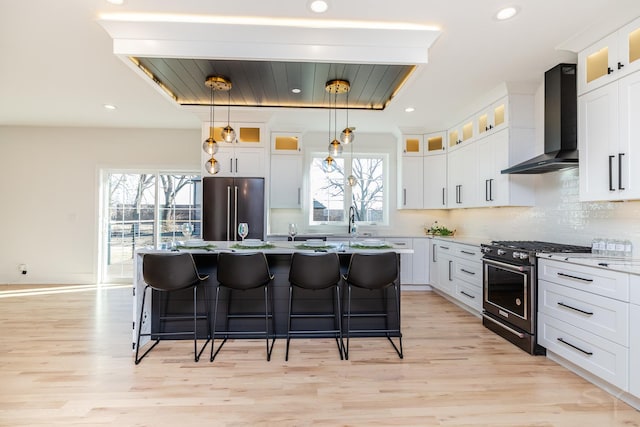 kitchen with backsplash, stainless steel range with gas stovetop, high quality fridge, wall chimney range hood, and a kitchen bar