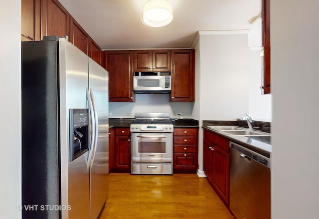 kitchen featuring stainless steel appliances, dark countertops, a sink, dark brown cabinets, and light wood-type flooring