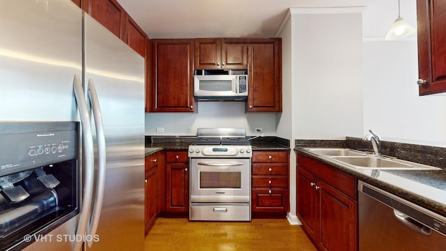 kitchen with a sink, appliances with stainless steel finishes, light wood-type flooring, reddish brown cabinets, and pendant lighting